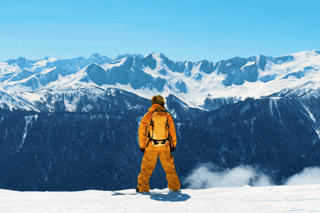 Сноубордист в желтом костюме на верхушке горы