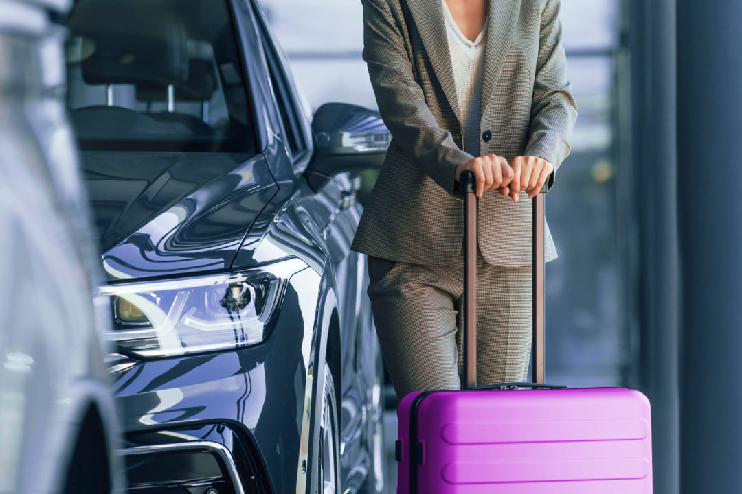 Девушка с фиолетовым чемоданом около машины