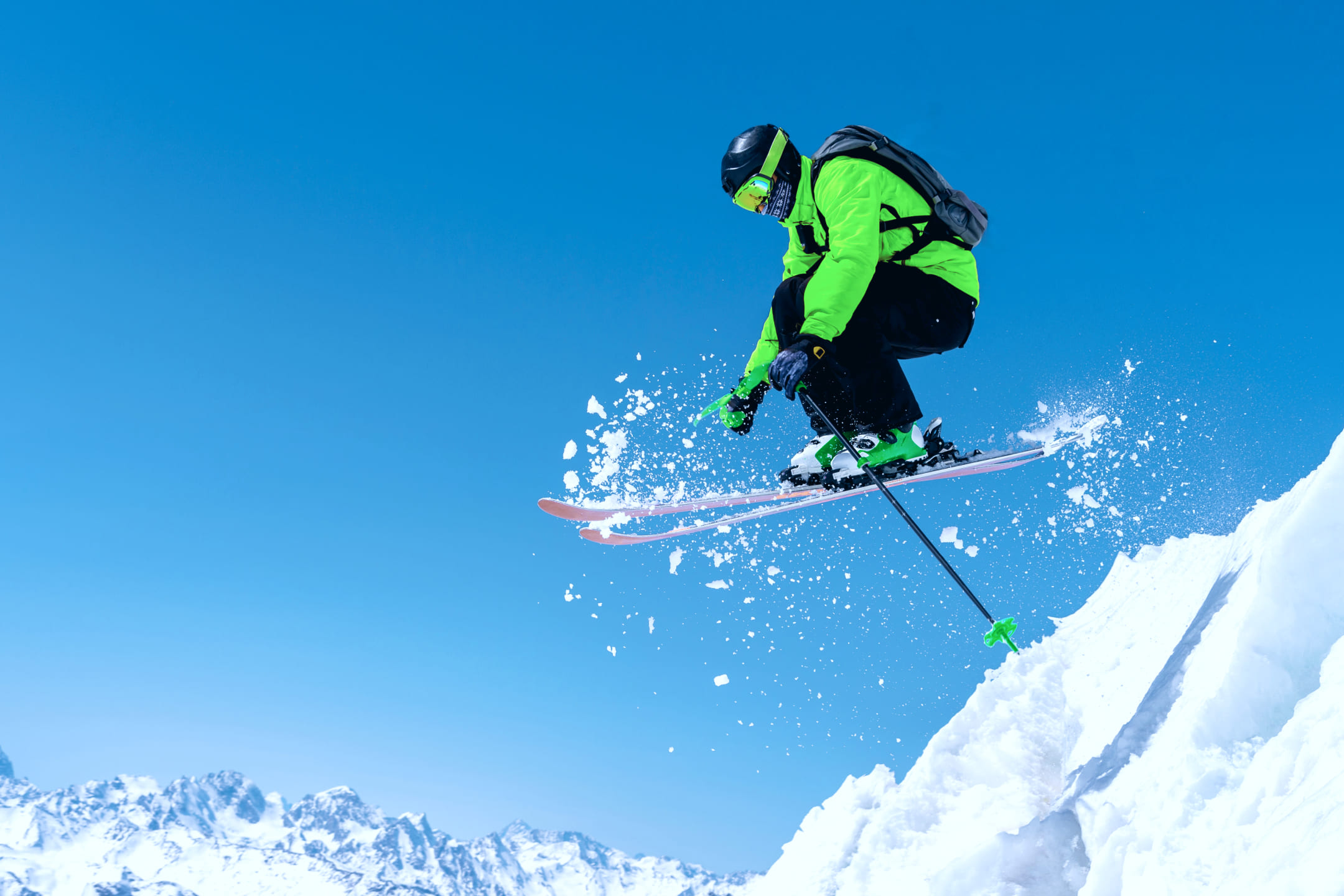 Лыжник в зеленой куртке катится с горы